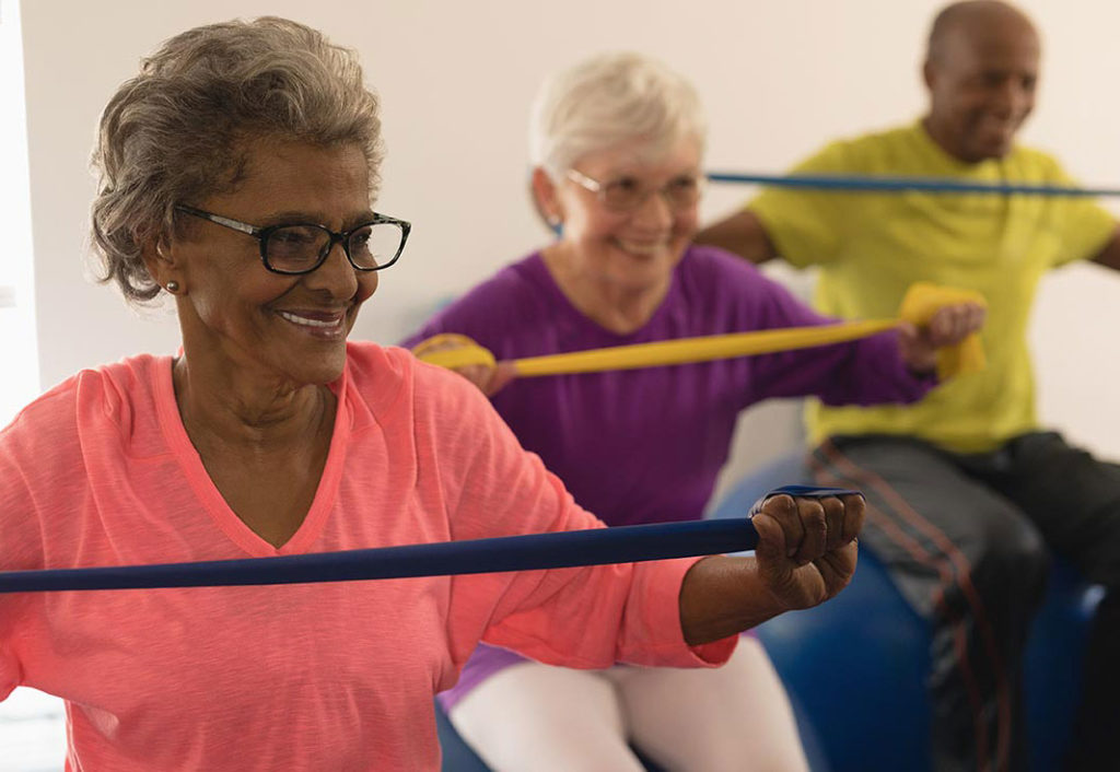 3 older adults sitting on yoga balls while using a resistance band for rehab exercise