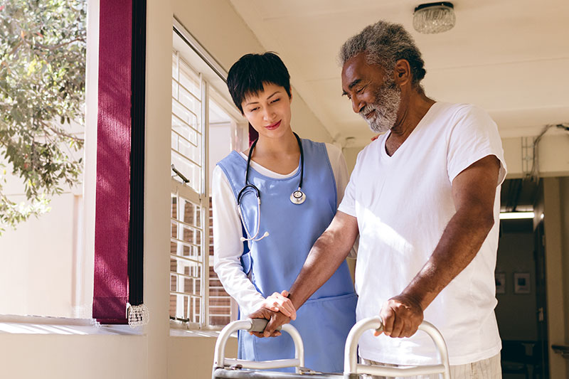 Senior African American man using a walker being assisted by a nurse