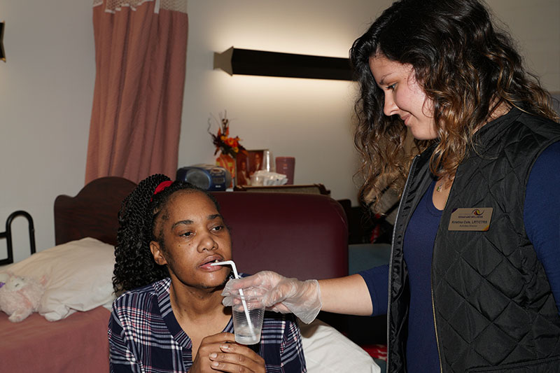 A East Carolina Health & Rehab staff member holding a cup assisting a patient to drink from a straw