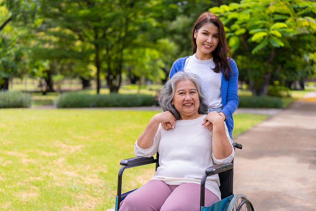 An elderly woman smiling in a wheel chair with her care giver standing behind her senior chronic wound care