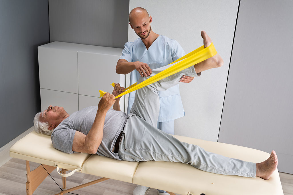 A Senior Man Using a Resistance Band to Stretch His Leg With Help From a Physical Therapist Short-Term Rehab for Seniors